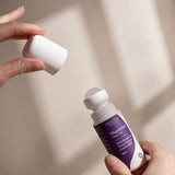 Hands removing the white cap from Amazing You Sleep Magnesium Gel 60ml, showing the roller ball and purple label in natural sunlight.