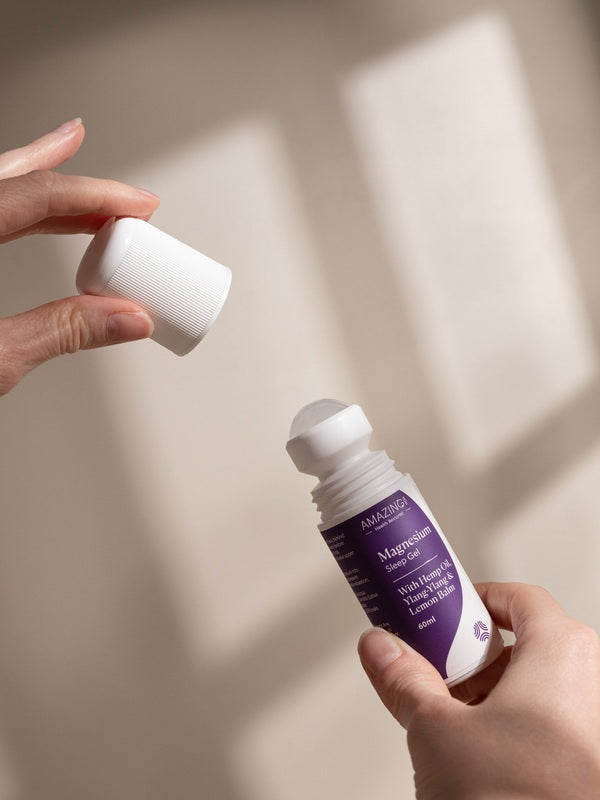 Hands removing the white cap from Amazing You Sleep Magnesium Gel 60ml, showing the roller ball and purple label in natural sunlight.