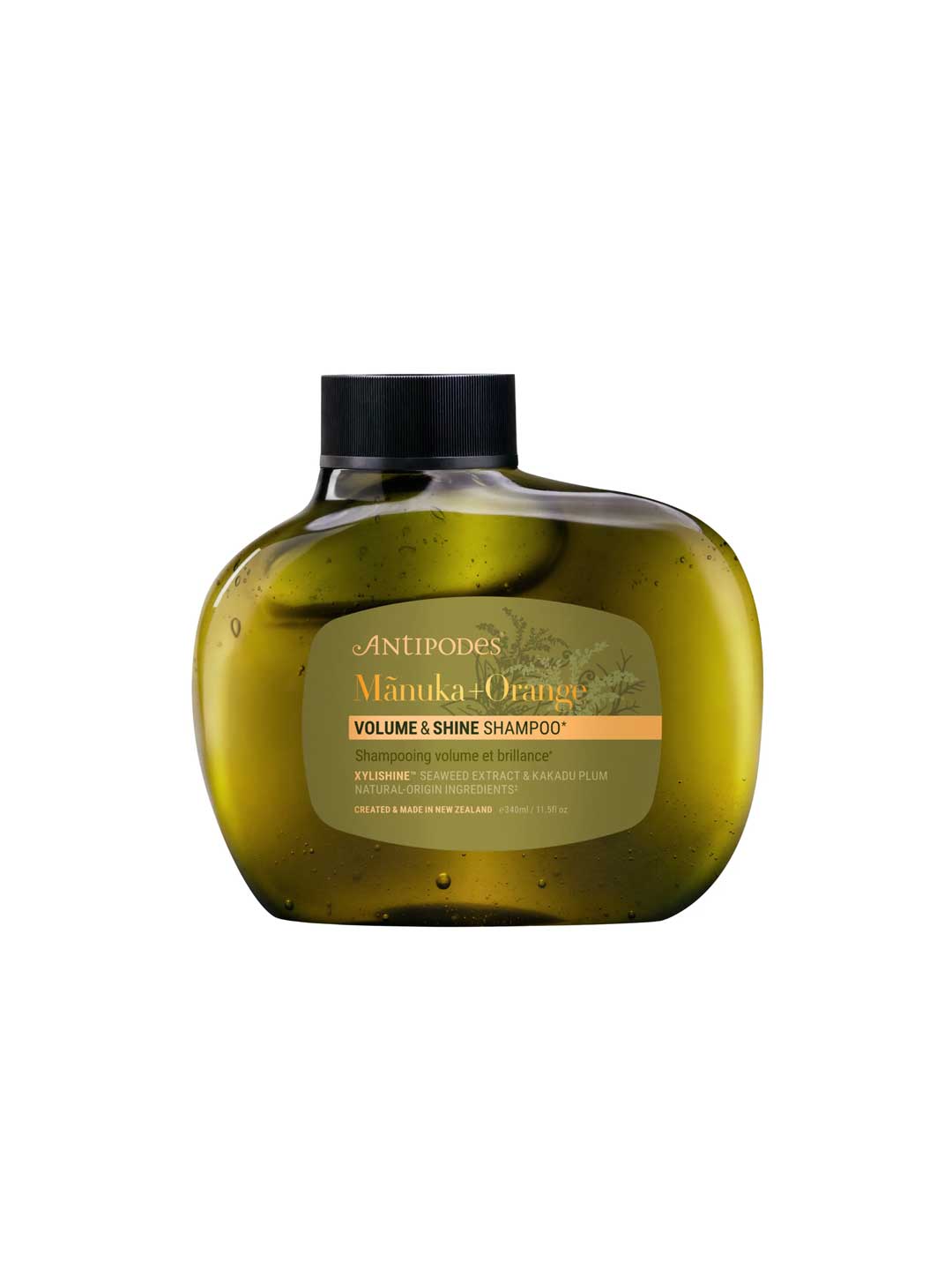 A green, oval bottle of Antipodes Manuka + Orange Volume & Shine Shampoo (340ml) features a black cap and beige label. This natural haircare essential boosts volume and shine with manuka and orange extracts.