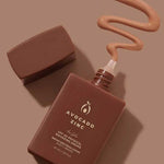 A brown bottle of Avocado Zinc SPF50 Physical Bronzing Drops 40ml with its cap off rests on a matching surface, with tinted mineral sunscreen swirled out to display its color and creamy texture.