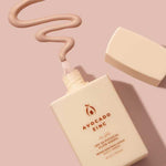 A bottle of Avocado Zinc SPF50 Physical Glow Drops 40ml in beige sits on a pink surface with the cap off, and the creamy product is dispensed in a wavy line above it.