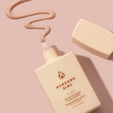 A bottle of Avocado Zinc SPF50 Physical Glow Drops 40ml in beige sits on a pink surface with the cap off, and the creamy product is dispensed in a wavy line above it.