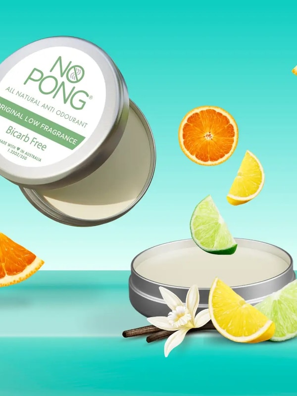 Open silver No Pong Original Low Fragrance Bicarb Free tins showing smooth pale balm against turquoise, surrounded by suspended citrus wedges, a white flower and dark vanilla-like pods.
