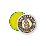 A round tin of Badger Balm Hardworking Hands 56g, lid partially open to show yellow balm inside. The lid displays a badger illustration and USDA Organic label, highlighting its use for dry hands.