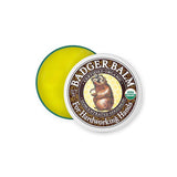 A round tin of Badger Balm Hardworking Hands 56g, lid partially open to show yellow balm inside. The lid displays a badger illustration and USDA Organic label, highlighting its use for dry hands.
