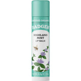 A 4.2g tube of Badger Lip Balm Highland Mint with a green cap features Certified Organic labeling, illustrations of mint leaves, purple flowers, and a bee. This refreshing mint balm hydrates and soothes your lips.