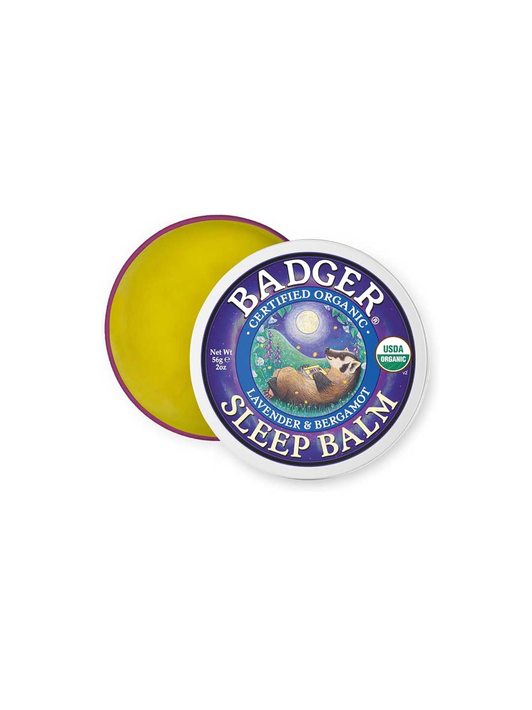 A 56g round tin of Badger Sleep Balm with the lid partially open, revealing yellow balm. The label shows a badger, lavender, bergamot, USDA organic seal, and highlights calming essential oils for restful nights.