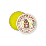 A partially open tin of Badger Unscented Healing Balm 56g reveals yellow balm inside. The lid displays a badger illustration and text stating certified organic and unscented—ideal for gentle, organic skin care.