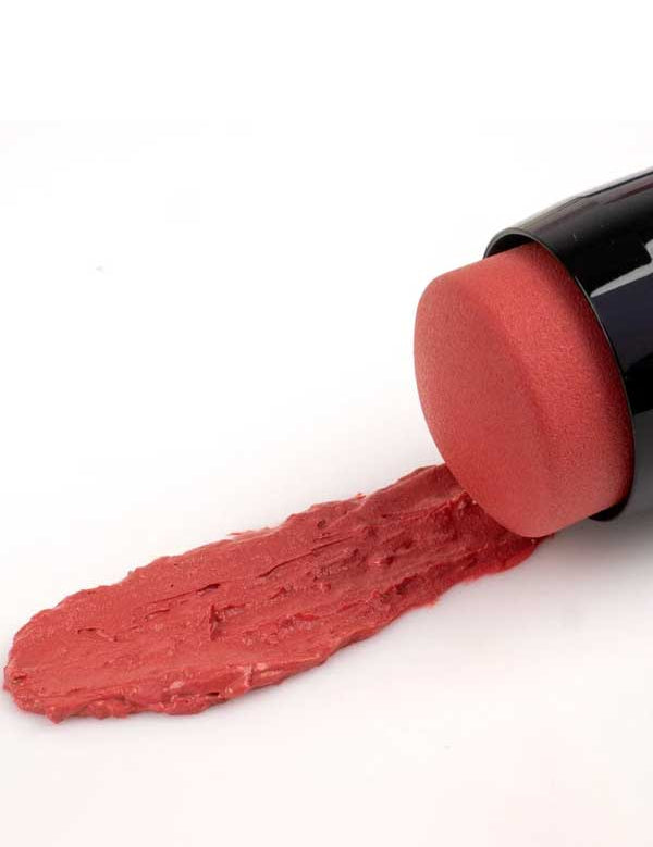 The Benecos Multi Stick - Be Peachy lies on its side, showcasing its pastel peach shade as the creamy pinkish-red product is smeared on a white surface.