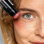 Model holding the Benecos Multi Stick in Be Pinky beside her eye, showing the rosy pink cream colour.