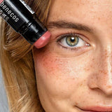 Model holding the Benecos Multi Stick in Be Pinky beside her eye, showing the rosy pink cream colour.