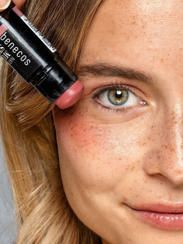 Model holding the Benecos Multi Stick in Be Pinky beside her eye, showing the rosy pink cream colour.