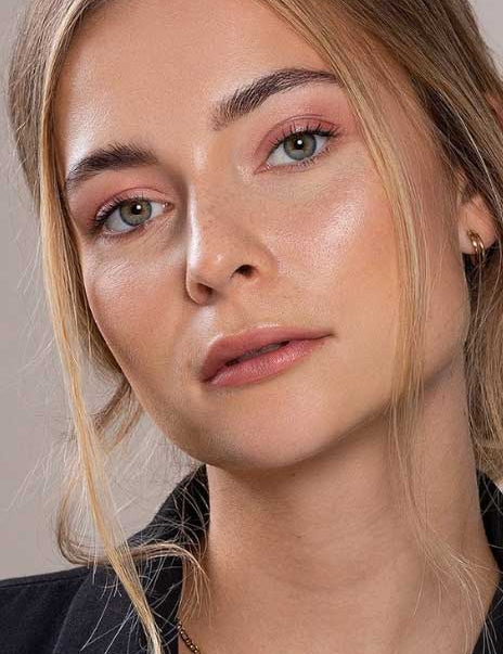Close-up of a young woman with fair skin, light hazel eyes, and blonde hair parted in the middle. She’s wearing natural vegan makeup with a hint of Benecos Beauty ID Palette Lip & Cheek Refill - Aperitif Kiss (matte raspberry red) and a black top.
