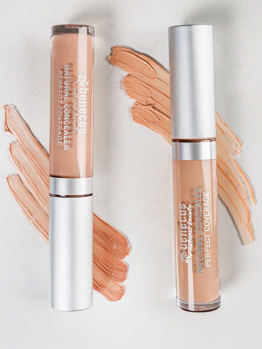Two tubes of Benecos Concealer 5ml stand upright on a white background, with swatches of this long-lasting formula in various shades displayed beside each tube.