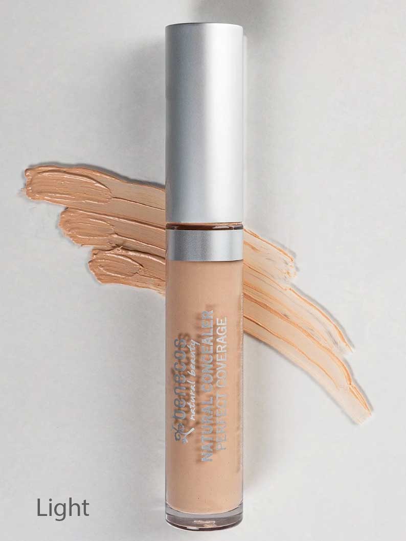 A 5ml tube of Benecos Concealer labeled Light with a silver cap stands before a swatch of its light beige shade on a gray background.