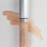 A 5ml tube of Benecos Concealer labeled Light with a silver cap stands before a swatch of its light beige shade on a gray background.