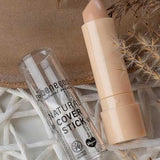 A beige Benecos Cover Stick 4.5g with its clear cap off sits on a woven white surface next to dried grasses. This high coverage concealer is vegan and certified organic by Benecos.