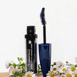 An open tube of Benecos Mascara Adorable Lashes Deep Ocean 5.5ml with a blue wand rests among white and yellow daisies on a light background, ideal for naturally lengthening lashes.