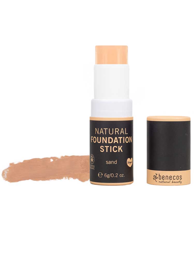 The Benecos Natural Foundation Stick 6g in Sand is shown uncapped, revealing the vegan, buildable organic stick foundation and a swatch beside its sleek black packaging with gold and white details.