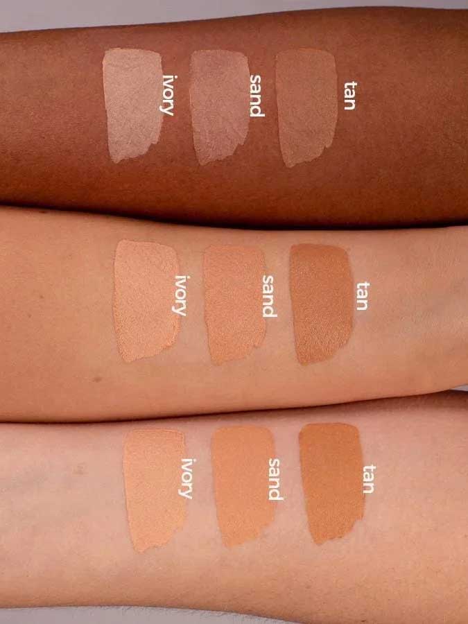 Three forearms of different skin tones display swatches of Benecos Natural Foundation Stick 6g in ivory, sand, and tan, demonstrating the buildable coverage these vegan shades offer across various complexions.