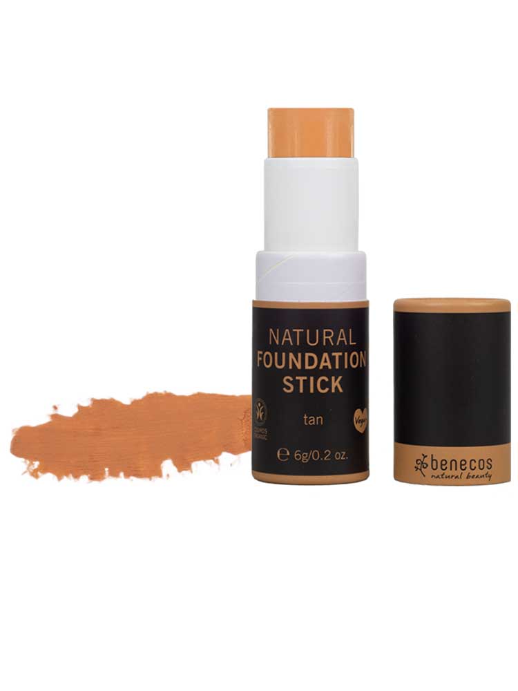The Benecos Natural Foundation Stick 6g in tan is displayed with the cap off, revealing the product and a swatch on the left. The cap lies nearby, emphasizing its buildable coverage and organic formula.