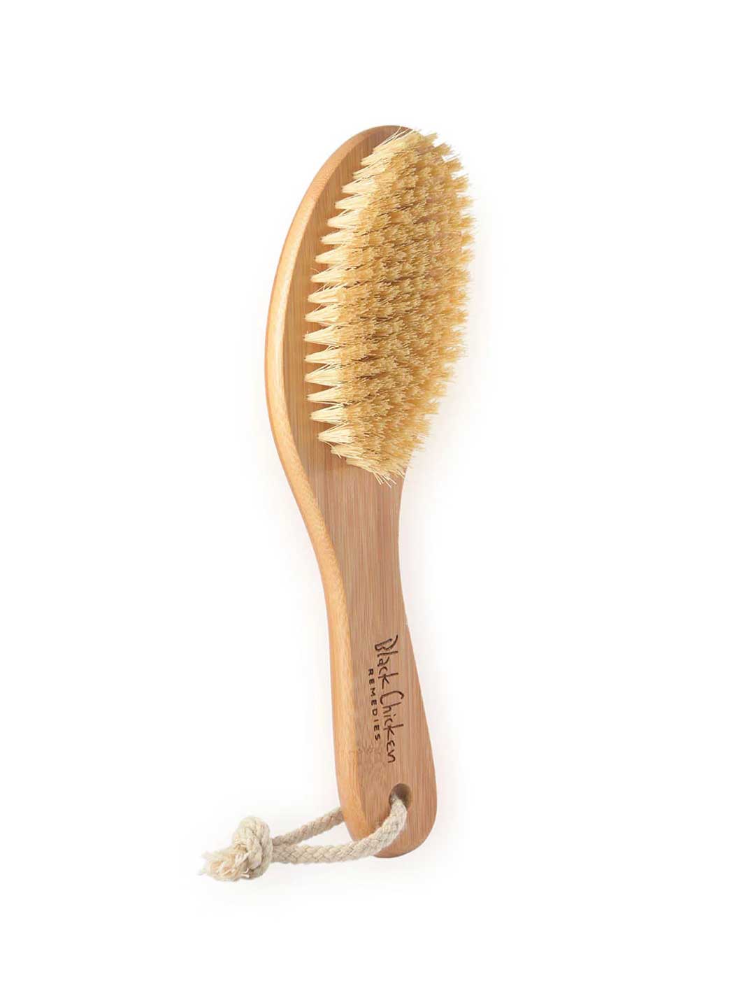 The Black Chicken Remedies Garshana Dry Body Brush features natural bristles, a wooden ergonomic handle with a rope loop for hanging, and is inspired by Ayurvedic wellness to boost lymphatic function. The brand name is printed on the handle.