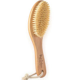 The Black Chicken Remedies Garshana Dry Body Brush features natural bristles, a wooden ergonomic handle with a rope loop for hanging, and is inspired by Ayurvedic wellness to boost lymphatic function. The brand name is printed on the handle.