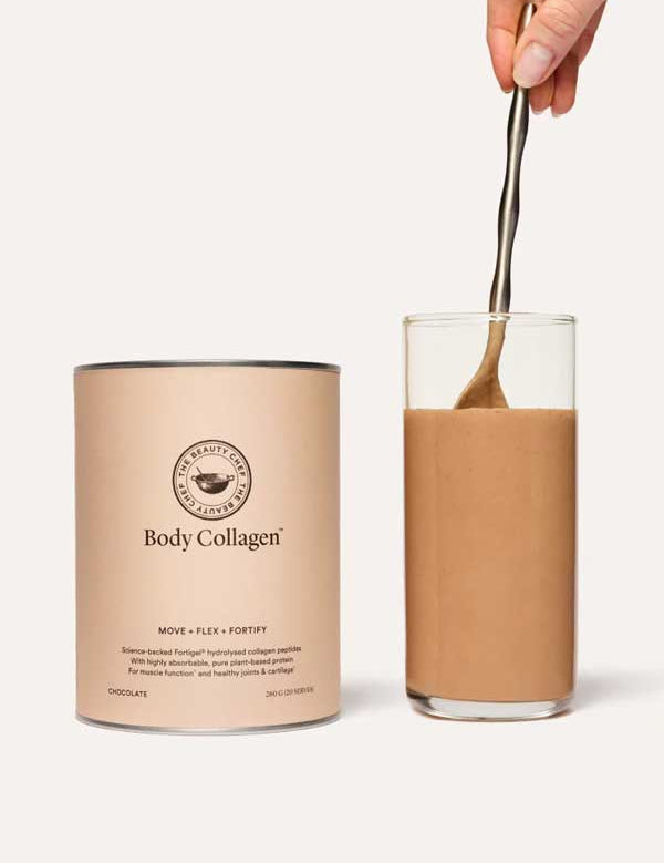 A hand stirs a creamy chocolate drink beside The Beauty Chef Body Collagen™ Chocolate 260g canister, which features collagen peptides for joint support and highlights its delicious chocolate flavor on the label.