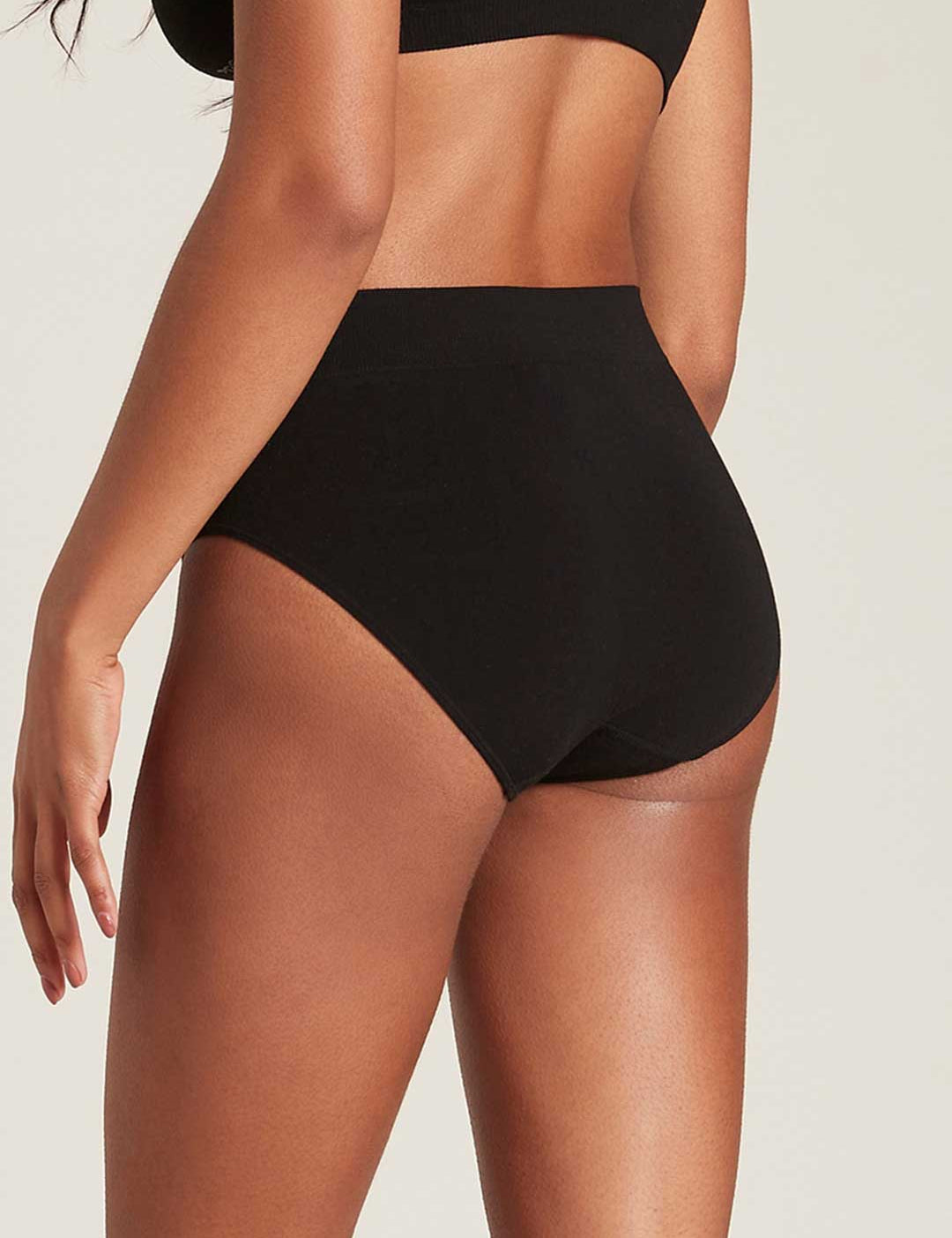 Three-quarter rear view of a model wearing black Boody Full Briefs, showing their high waist and full back coverage.