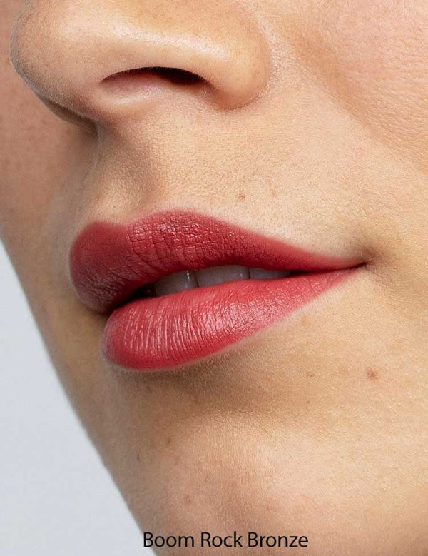 Close-up of lips with fair, freckled skin wearing Antipodes Moisture Boost Natural Lipsticks 4g in a warm bronze shade and satin finish. The text "Boom Rock Bronze" is displayed at the bottom.