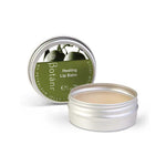 A silver metal tin of Botân Healing Lip Balm, with the lid leaning behind the open tin showing the beige balm inside. The lid features a green label with botanical illustrations.