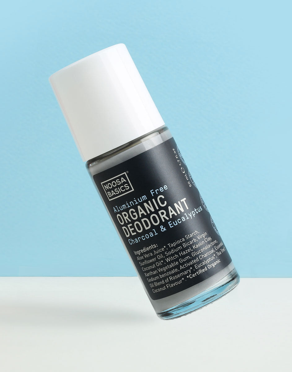 Clear Noosa Basics Charcoal and Eucalyptus roll-on deodorant bottle with a black label and white cap tilted diagonally against a pale blue background.