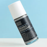 Clear Noosa Basics Charcoal and Eucalyptus roll-on deodorant bottle with a black label and white cap tilted diagonally against a pale blue background.