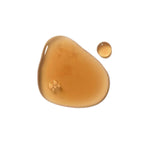 A glossy amber puddle of Dr Hauschka Clarifying Steam Bath liquid with a small separate round drop on white.