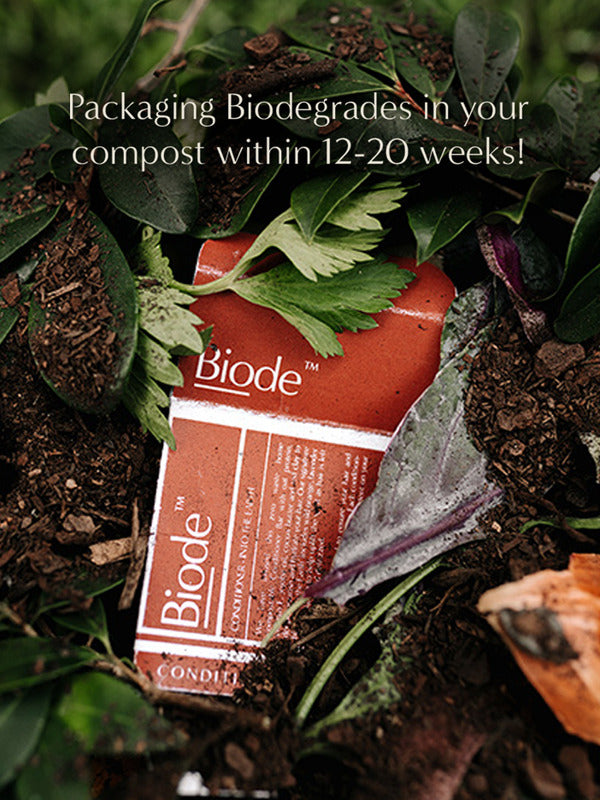 Terracotta Biode Into the Earth conditioner packaging among leaves and compost. Overlaid text states that the packaging biodegrades in compost within 12–20 weeks.