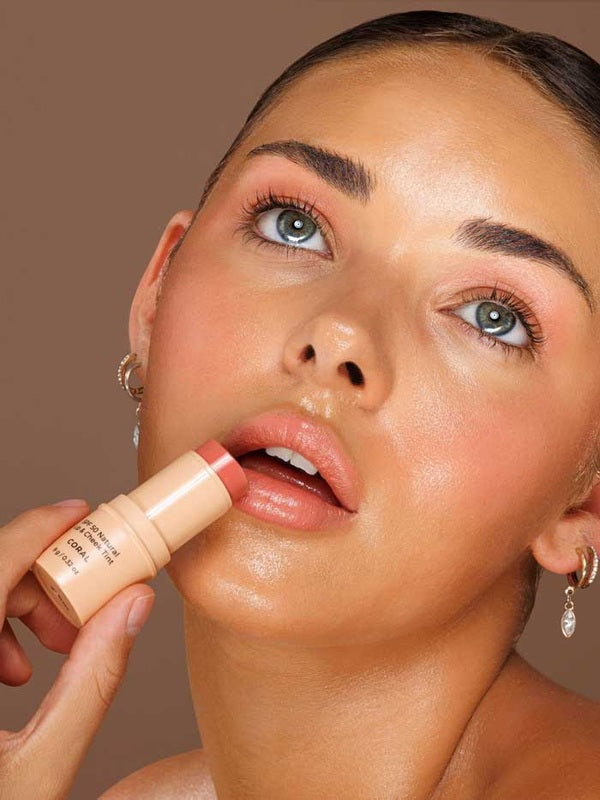 Model applying Avocado Zinc SPF50 Natural Lip & Cheek Tint in Coral directly to her lips.