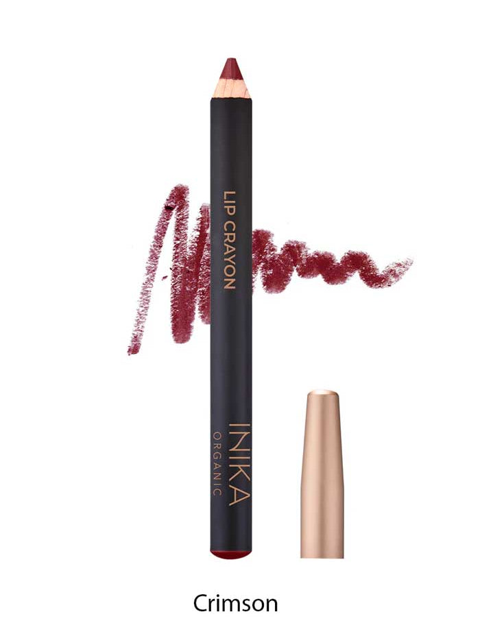 A crimson INIKA Organic Lip Crayons 6.7g with a color swatch behind it, labeled LIP CRAYON and INIKA ORGANIC. A gold cap sits beside it, while "Crimson" below highlights this long-lasting organic lip liner.