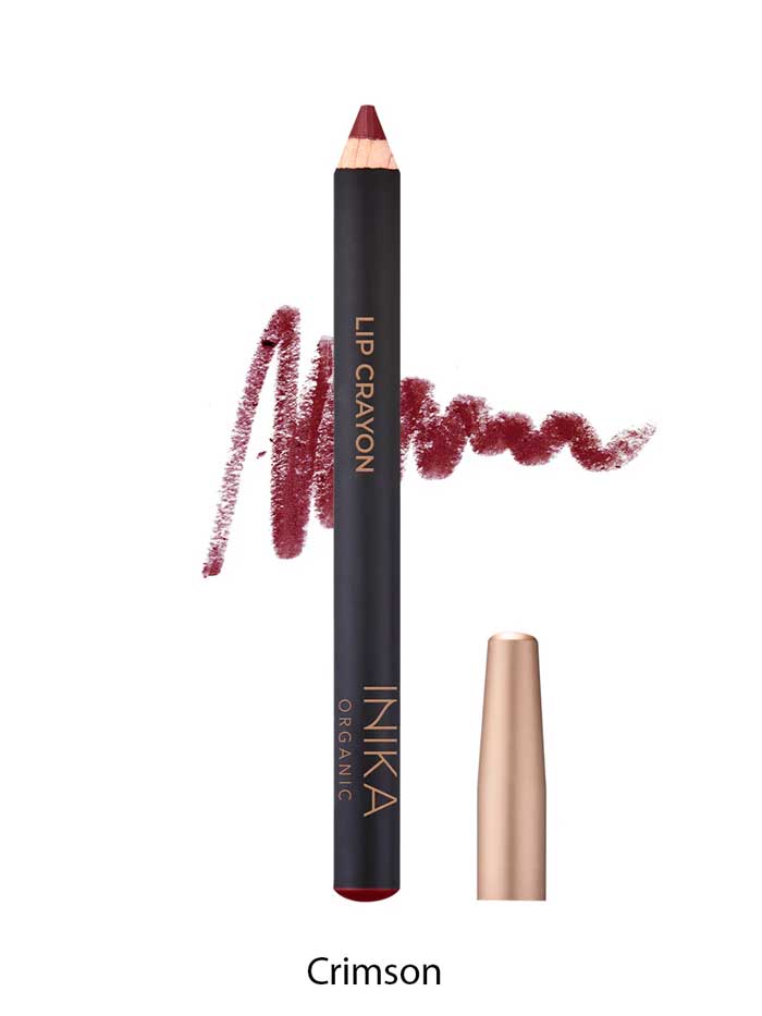 A crimson INIKA Organic Lip Crayons 6.7g with a color swatch behind it, labeled LIP CRAYON and INIKA ORGANIC. A gold cap sits beside it, while "Crimson" below highlights this long-lasting organic lip liner.