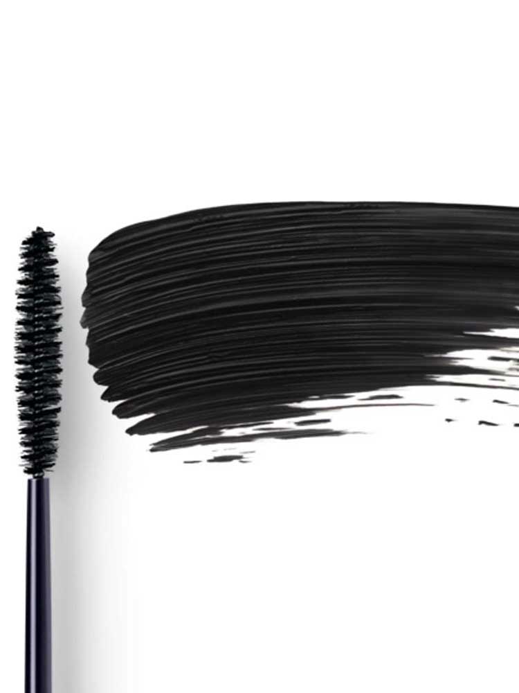 Dr Hauschka Defining Mascara 6ml is pictured with its black-bristled wand lying next to a bold swipe of defining black mascara on a white background.