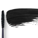 Dr Hauschka Defining Mascara 6ml is pictured with its black-bristled wand lying next to a bold swipe of defining black mascara on a white background.