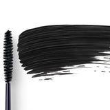 Dr Hauschka Defining Mascara 6ml is pictured with its black-bristled wand lying next to a bold swipe of defining black mascara on a white background.