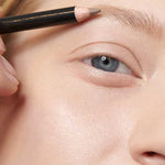A close-up shows a person with fair skin applying Dr Hauschka Eyebrow Definer 1.05g to their eyebrow. The pencil is held above the brow. Text below reads: Colour: 01 light brown.