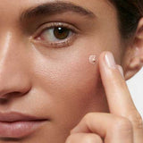 A close-up of a person applying Dr Hauschka Illuminating Fluid 30ml under their eye with a fingertip, creating a natural glow.