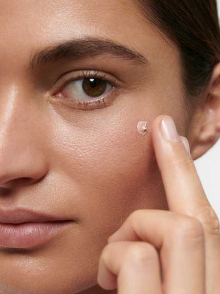 A close-up of a person applying Dr Hauschka Illuminating Fluid 30ml under their eye with a fingertip, creating a natural glow.