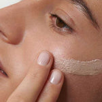 A close-up of someone applying Dr Hauschka Illuminating Fluid 30ml to their cheek with their fingers, highlighting the gentle application and natural glow for radiant, healthy-looking skin.