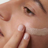 A close-up of someone applying Dr Hauschka Illuminating Fluid 30ml to their cheek with their fingers, highlighting the gentle application and natural glow for radiant, healthy-looking skin.