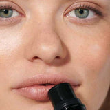 A close-up of a person applying Dr Hauschka Lip to Cheek Tint & Highlighter - Gold 6.1g to their lips, with clear skin and green eyes, showcases its gold shimmer and versatile use for both lips and cheeks.