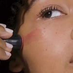 A person applies Dr Hauschka Lip to Cheek Tint - Rosewood 6.1g to their cheek with a makeup stick, showing only the upper face and the natural multi-purpose tint.