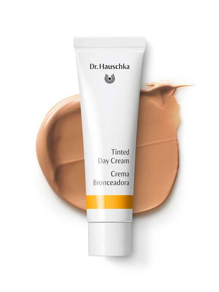 The Dr Hauschka Tinted Day Cream 30ml in a white tube rests on a beige cream smear, with branding and product name visible—ideal for achieving a natural glow with this tinted moisturiser.
