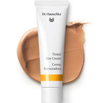 The Dr Hauschka Tinted Day Cream 30ml in a white tube rests on a beige cream smear, with branding and product name visible—ideal for achieving a natural glow with this tinted moisturiser.